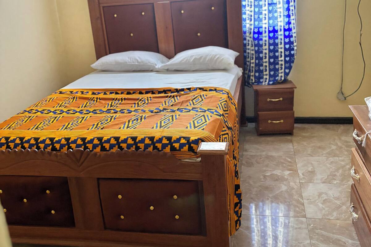 A bedroom with a wooden bed, a nightstand, a dresser, and a window with curtains.