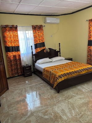Une chambre à coucher avec un lit, des rideaux, une table de chevet, une lampe et un appareil de climatisation.
