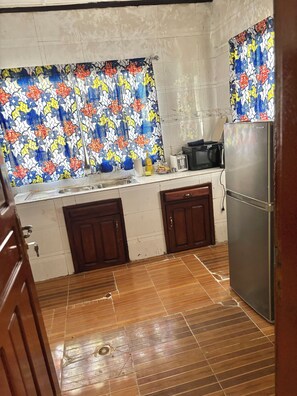 A kitchen with a tiled backsplash, wooden cabinets, a refrigerator, and a microwave. - BLM Lodge (Monrovia)