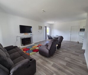 A living room with a fireplace, a television, and a dining area with chairs. - Quiet Hidden Cottage (Nulsen)