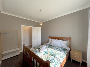 A bedroom with a bed, a nightstand, a wooden wardrobe, a hanging rack, and a door. - Quiet Hidden Cottage (Nulsen)