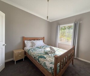 A bedroom with a bed, a nightstand, a window with curtains, and a door. - Quiet Hidden Cottage (Nulsen)