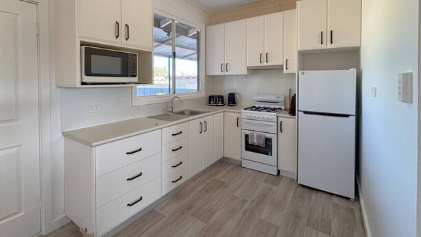 Cocina compacta con armarios blancos, microondas, estufa y refrigerador.
