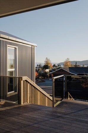 Un bĂątiment moderne dotĂ© dâune terrasse en bois, dâune porte vitrĂ©e et offrant une vue sur un quartier rĂ©sidentiel, avec des arbres et une montagne au loin.