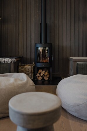 A cozy room with a wood-burning stove, a wicker basket, and two round ottomans.