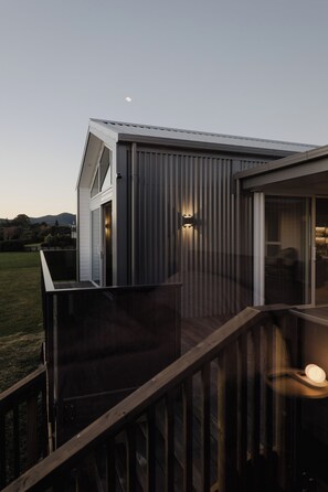 A modern building with a deck, a glass door, and two wall-mounted lights.