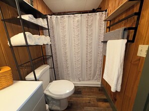 Un baño pequeño con inodoro, cortina de ducha y estante con toallas.