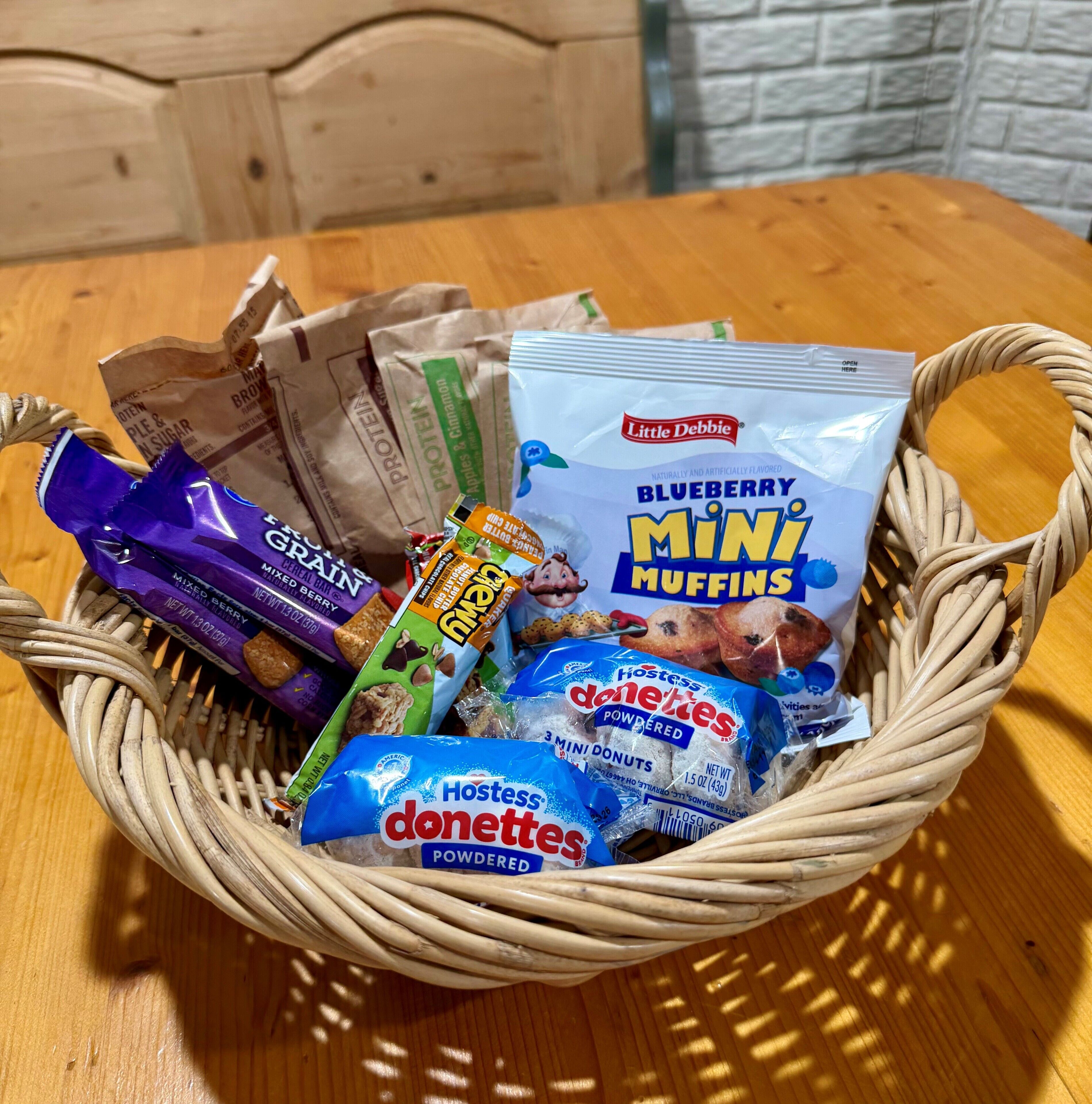 A basket containing various food items including cereal, protein bars, and packaged snacks.
