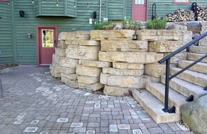 A stone retaining wall with steps leading up to a door, a brick pathway, and a green building with a red door. -  GrünHaus a peaceful private suite B&B in charming Frankenmuth (Frankenmuth)
