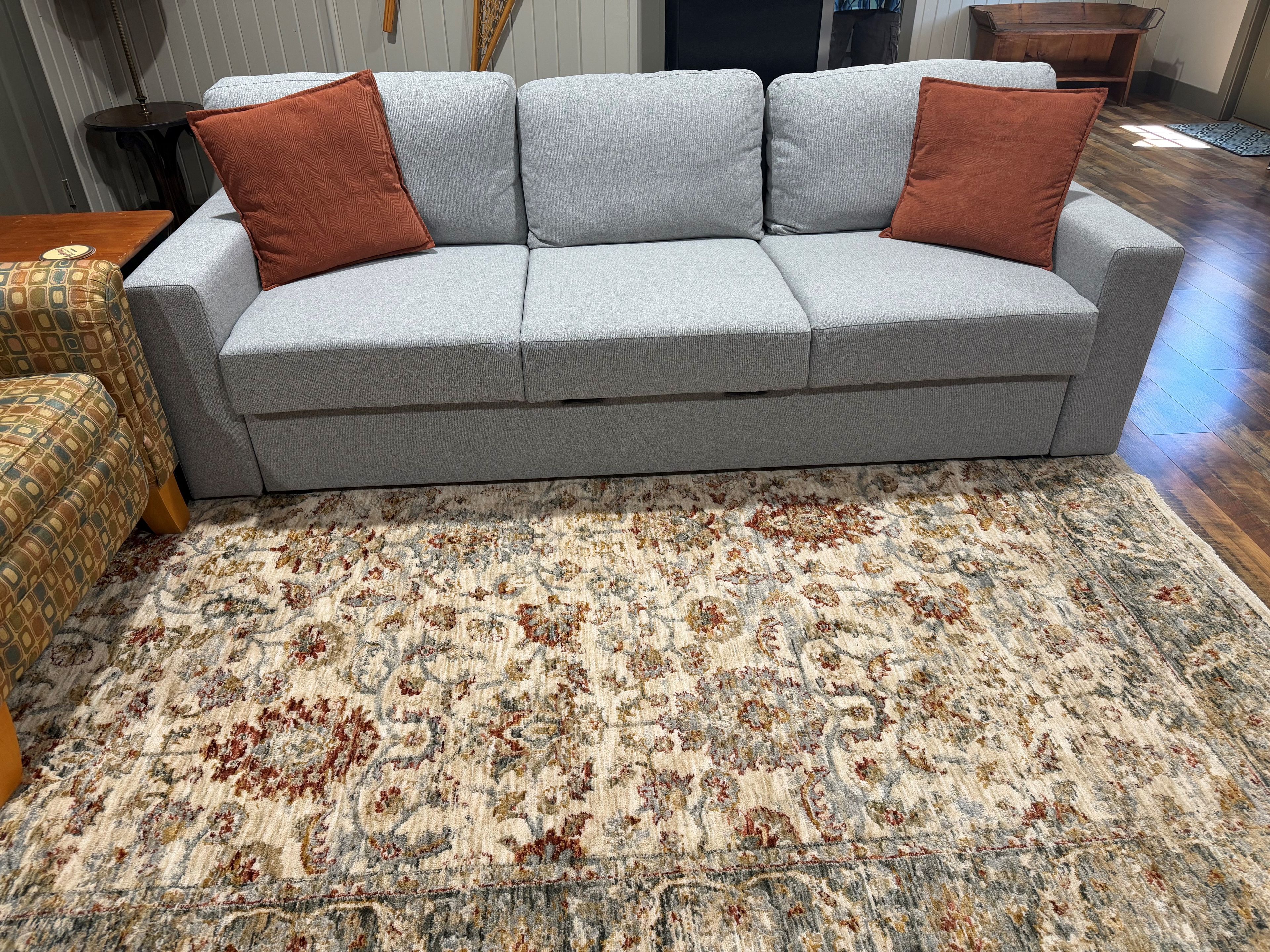 A grey sofa with two brown cushions, a patterned rug, and a wooden coffee table.