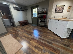 A kitchen with wooden flooring, white cabinets, a bench, and a coffee station.