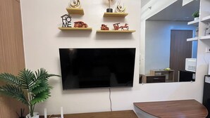 Una sala de estar moderna con televisor de pantalla plana, muebles de madera, objetos decorativos en estantes y una planta en maceta.