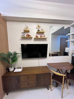 Un salon moderne avec un téléviseur à écran plat, des meubles en bois, des objets décoratifs disposés sur des étagères et une plante en pot.