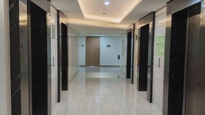 A corridor with elevators, a door at the end, and a ceiling with recessed lighting. - Chino Roces Makati - PAID Parking - Red Residences (Makati City)