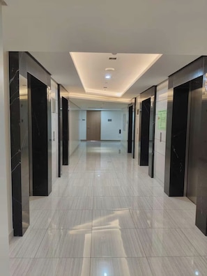 Un pasillo con ascensores, una puerta al final y un techo con iluminación empotrada.