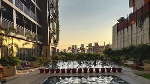 Una piscina con una escalera de metal, rodeada de plantas en macetas y un paisaje urbano al fondo.