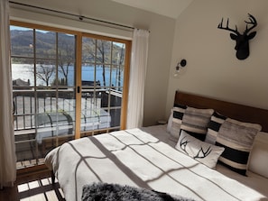 A bedroom with a bed, a view of a lake, a deer head decoration, and a nightstand.
