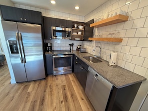 A modern kitchen with stainless steel appliances, a dishwasher, and a wooden floor.