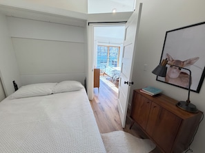 A bedroom with a bed, a wooden cabinet, a desk with a lamp, and a door leading to a balcony.