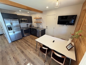 A modern kitchen with stainless steel appliances, a dining table, and a TV mounted on the wall.