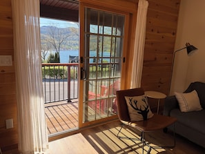 A wooden cabin with a sliding glass door leading to a balcony with a view of a lake and mountains.