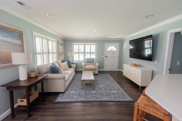 A living room with a sofa, armchairs, a coffee table, and a TV. There are windows with blinds, a door, and a patterned rug. - Downtown Conway 3 bedroom home in picturesque neighborhood (Conway)
