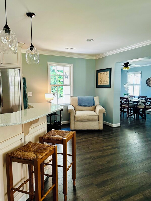 A kitchen with a refrigerator, a dining area with a table and chairs, a chair with a blue throw, and a wooden stool.