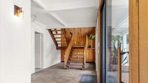 Un intérieur spacieux avec un escalier en bois, un revêtement de sol en pierre et une porte vitrée donnant sur l’extérieur.