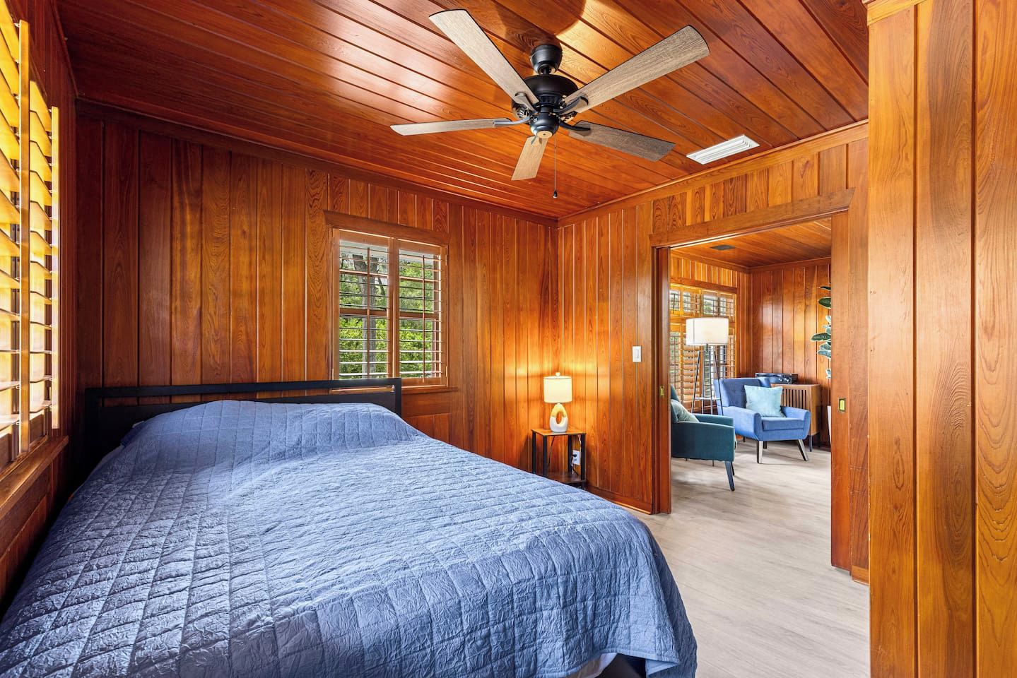Un dormitorio con una cama, ventilador de techo y ventana con persianas.