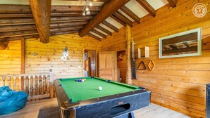 Een pooltafel in een houten ruimte met een houten plafond en wanden, een deur en een lijst met een afbeelding aan de muur.