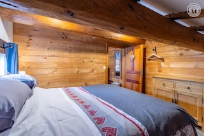 A wooden cabin room with a bed, a wardrobe, and a door leading to another room. - The Chalet Des Sangliers (SEEZ)