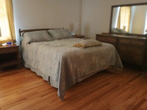 Ein Schlafzimmer mit Bett, Holzboden, Nachttischen, Kommode und Spiegel.