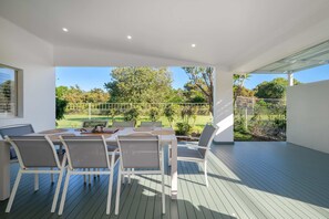 Eine moderne Außenpatio mit Esstisch und Stühlen, umgeben von einem weißen Zaun und Grünpflanzen.