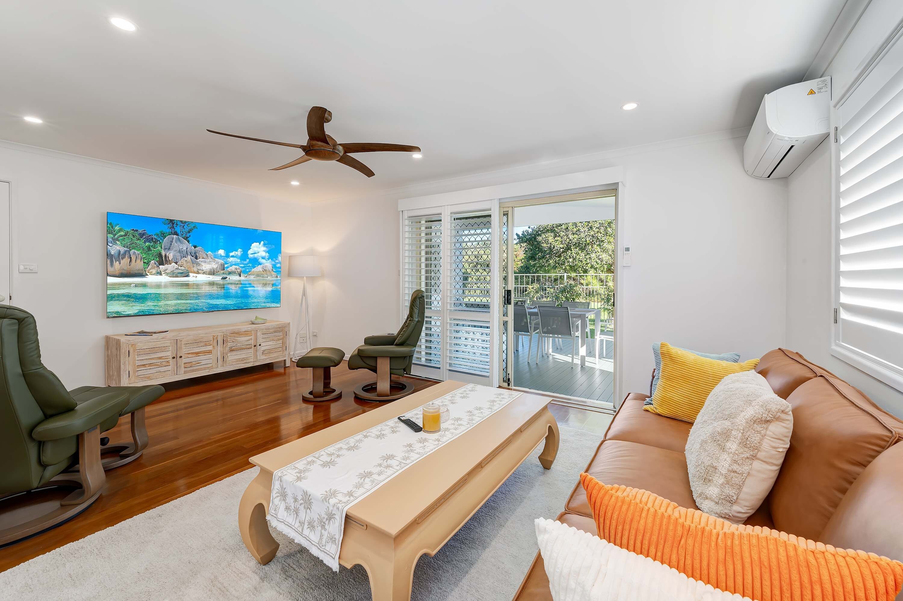 A living room with a TV, seating, a ceiling fan, and a sliding glass door leading to an outdoor area.