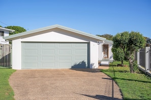 A single-story house with a light green garage door, a small porch, and a tree in the yard. - Alice by the Lake Currimundi (Currimundi)