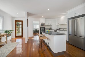 A modern kitchen with white cabinets, stainless steel appliances, and a central island with stools. - Alice by the Lake Currimundi (Currimundi)