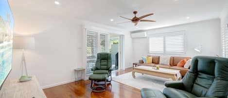 A spacious living room with a ceiling fan, a sofa, a recliner, and a coffee table.