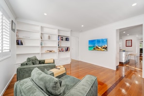 A modern living room with a green sofa, white shelving, and a painting of a beach scene. - Alice by the Lake Currimundi (Currimundi)