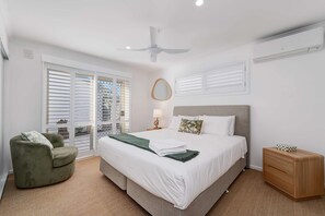 A bedroom with a bed, a chair, a nightstand, a ceiling fan, and a window with blinds. - Alice by the Lake Currimundi (Currimundi)