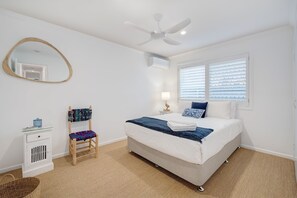 A bedroom with a bed, a chair, a bedside table, a lamp, a ceiling fan, and a window with blinds. - Alice by the Lake Currimundi (Currimundi)