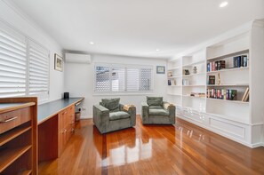Et værelse med to grønne lænestole, et træskrivebord, en bogreol og et vindue med persienner.