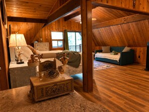 A wooden interior with a bed, a sofa, a lamp, and a decorative box. - Grand River Cabin I Fire Pit I Deck I Pool Table (East Stroudsburg)