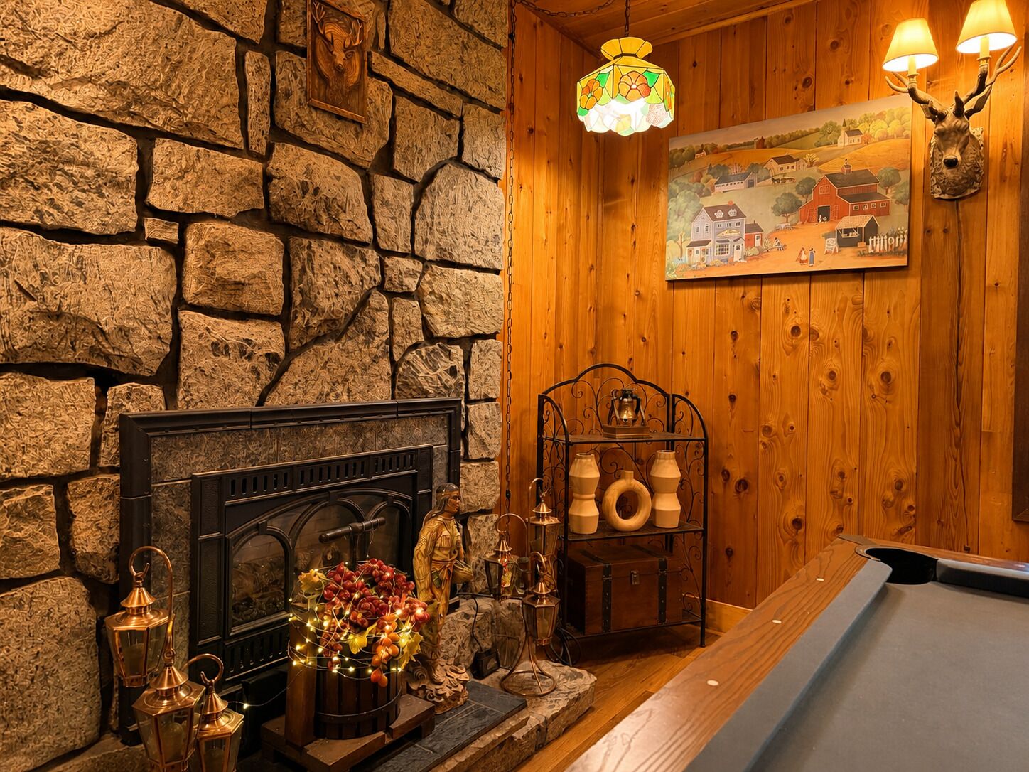 Une pièce avec un mur en pierre, un lambris en bois, une cheminée, une table de billard et un tableau accroché au mur.