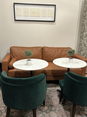 A brown leather sofa with two white marble tables, each with a small potted plant.