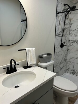 Une salle de bain avec un lavabo blanc, un robinet noir, des toilettes blanches et un espace douche avec un mur en marbre.