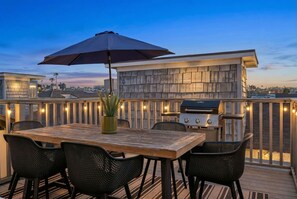 Eine Dachterrasse mit Holztisch, vier Stühlen, einem Grill und Lichterketten.