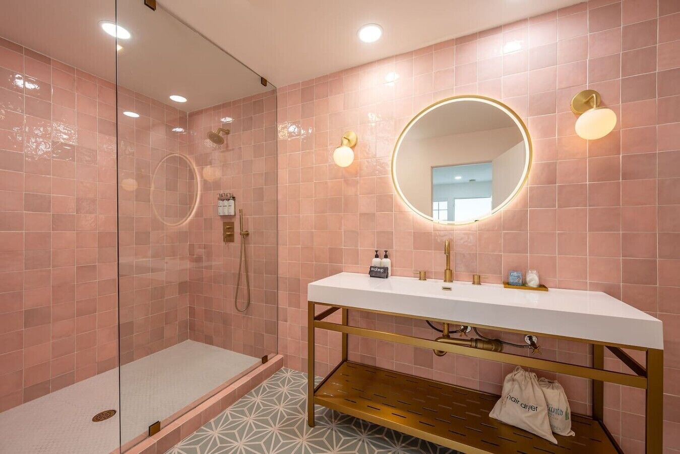 Une salle de bain moderne avec une douche à parois de verre, un meuble-lavabo blanc doté de robinetterie dorée et des murs recouverts de carreaux roses.