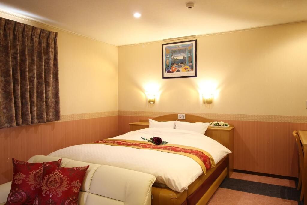 Une chambre d’hôtel comprenant un lit, une table de chevet, une chaise, un tableau au mur et deux lampes fixées au mur.