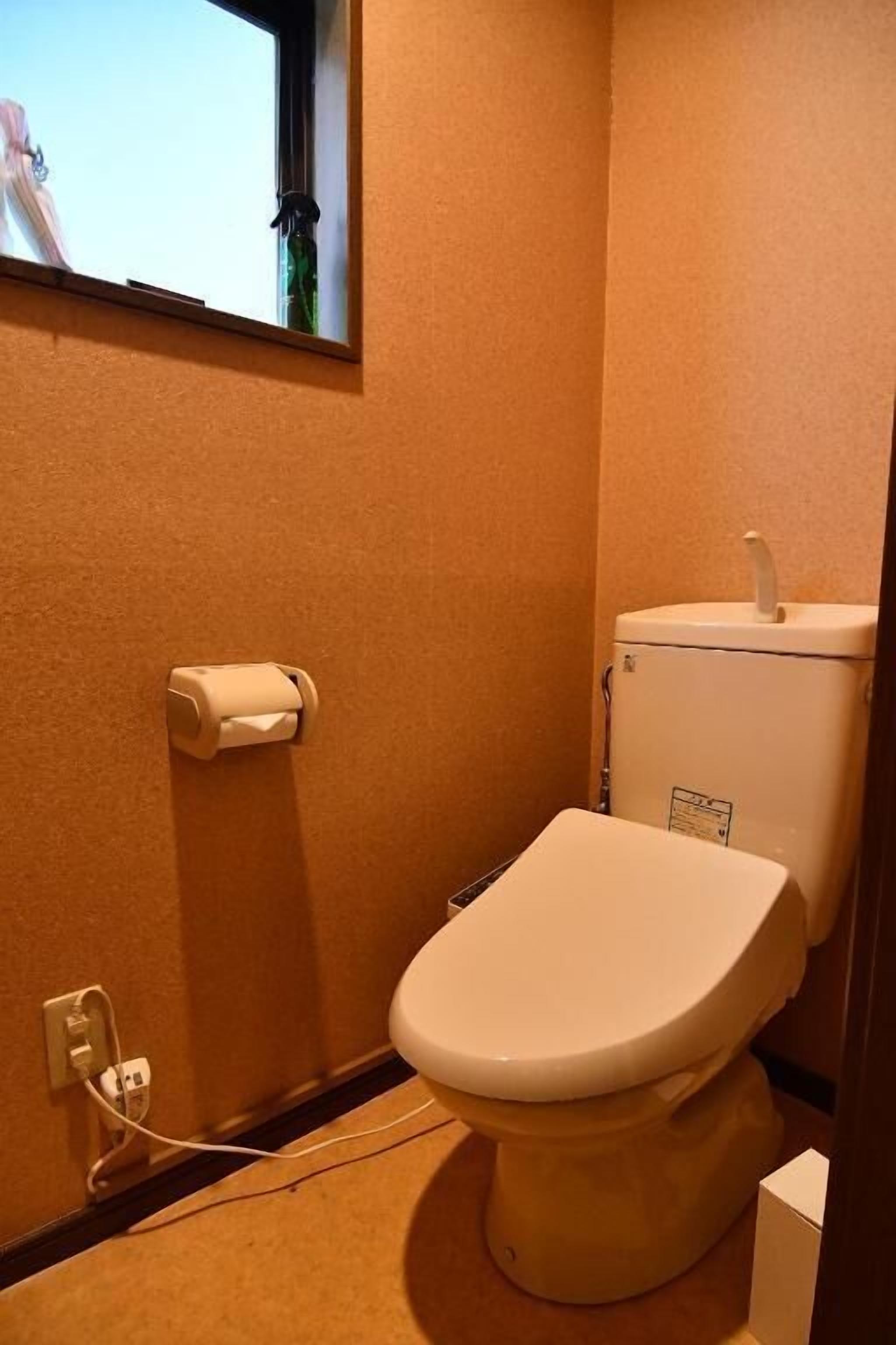 A small bathroom with a toilet, a roll of toilet paper, and a window above the toilet.