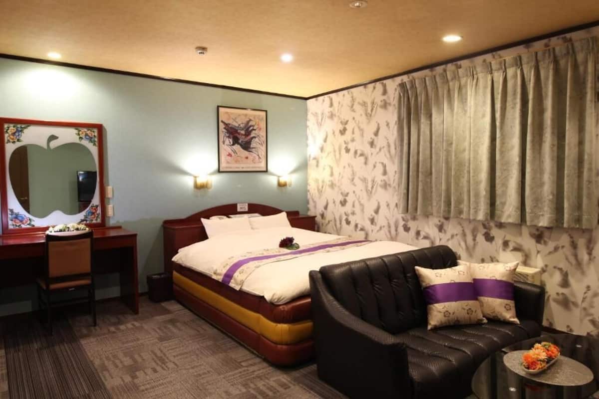 Una habitación de hotel con cama, escritorio, silla, sofá y una pequeña mesa con flores.